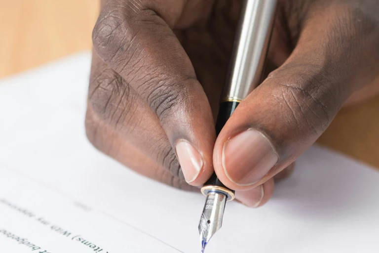 A Black person's hand seen holding a pen to paper.