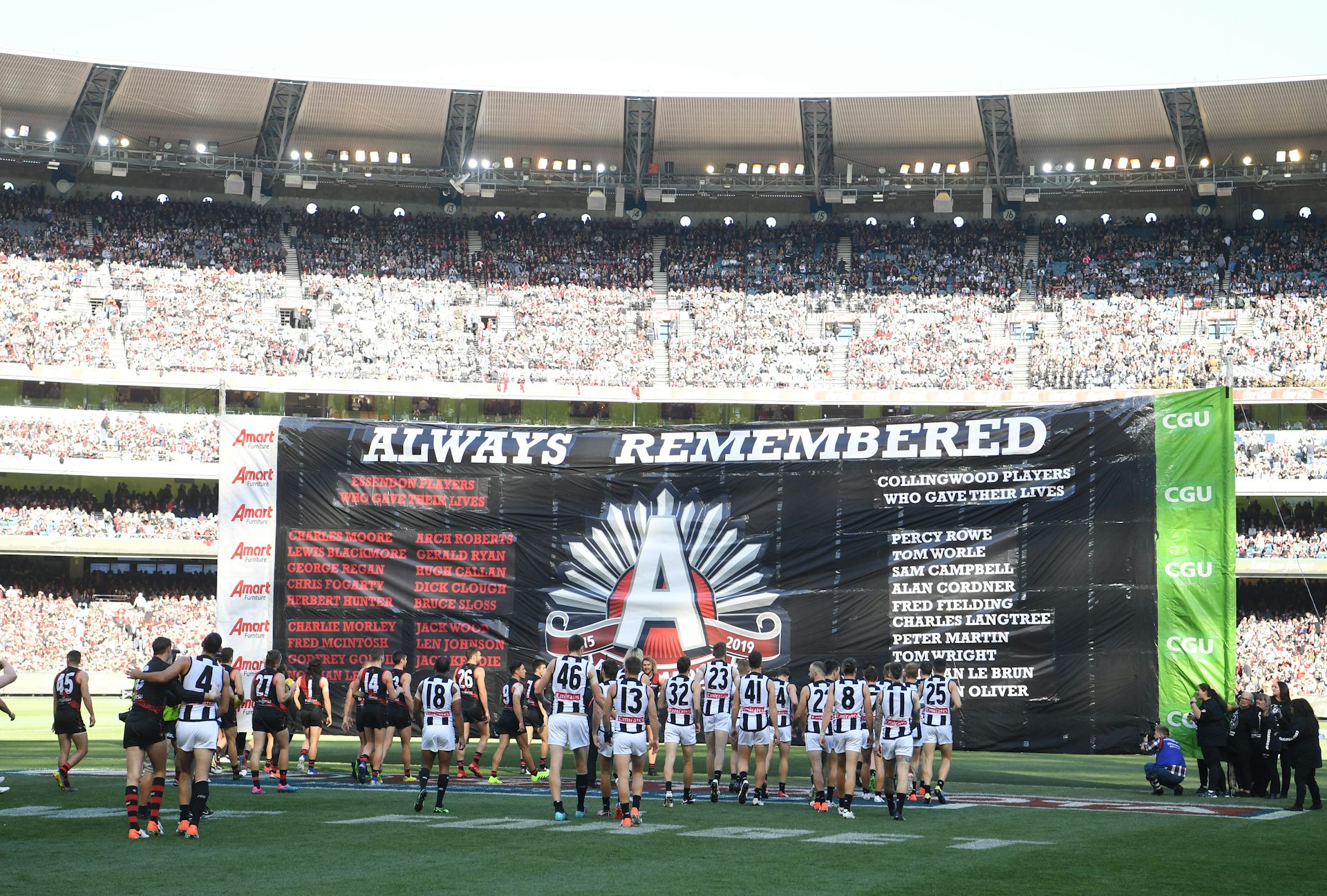 Essendon and Collingwood players prepare to run through a shared banner before an Anzac Day game.