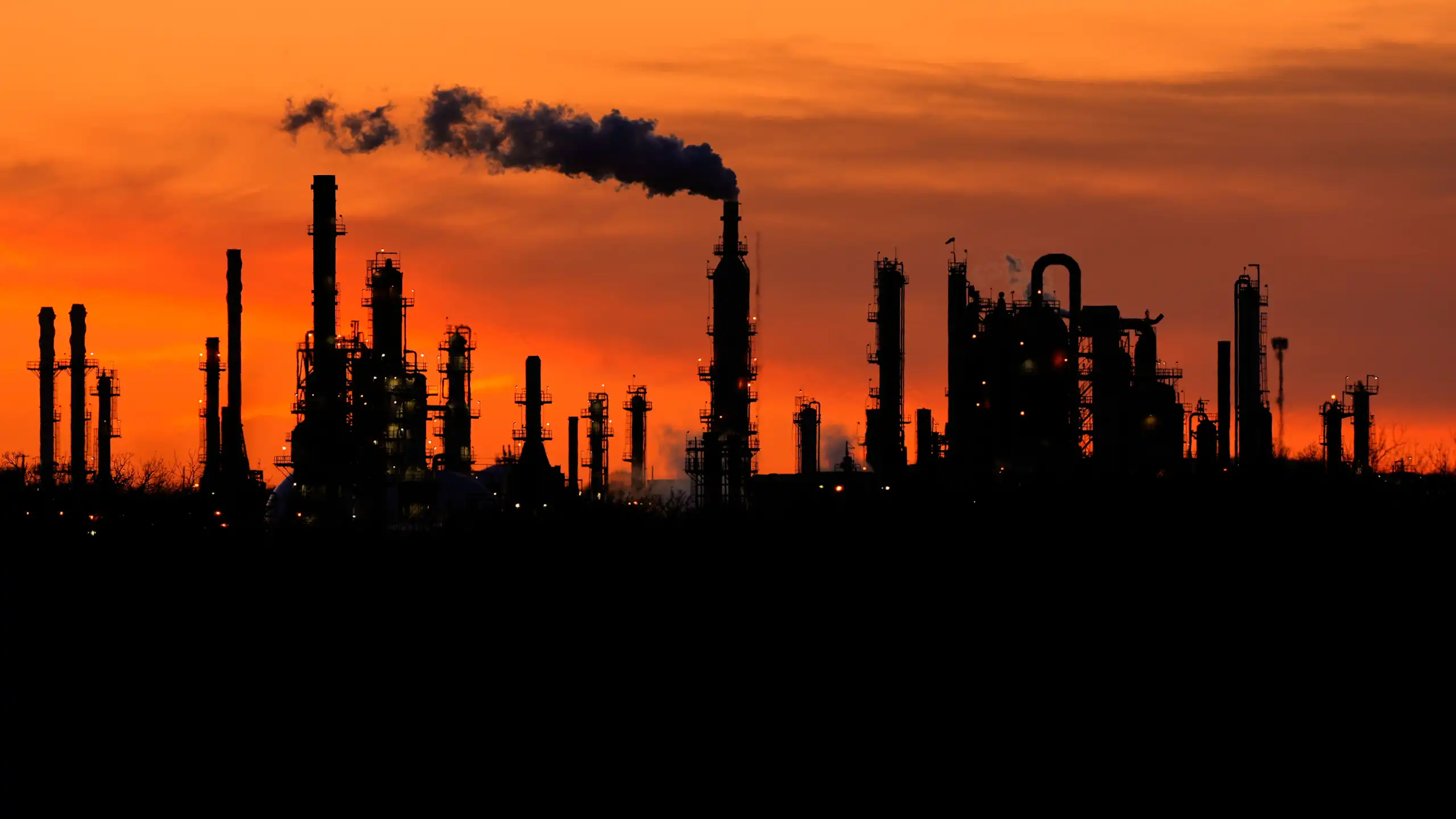 smoke stacks at an industrial plant silhouetted by an orange sky at sunset