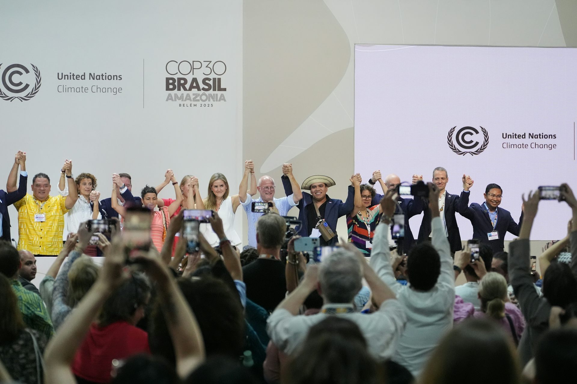 Las personas en una sala grande se paran juntas y levantan la mano, otras miran.