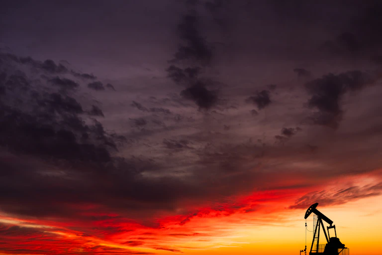 single oil pump-jack against sunset sky.