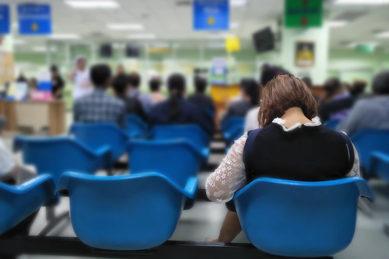 A busy hospital waiting room. I woman sits in the furthest row back.