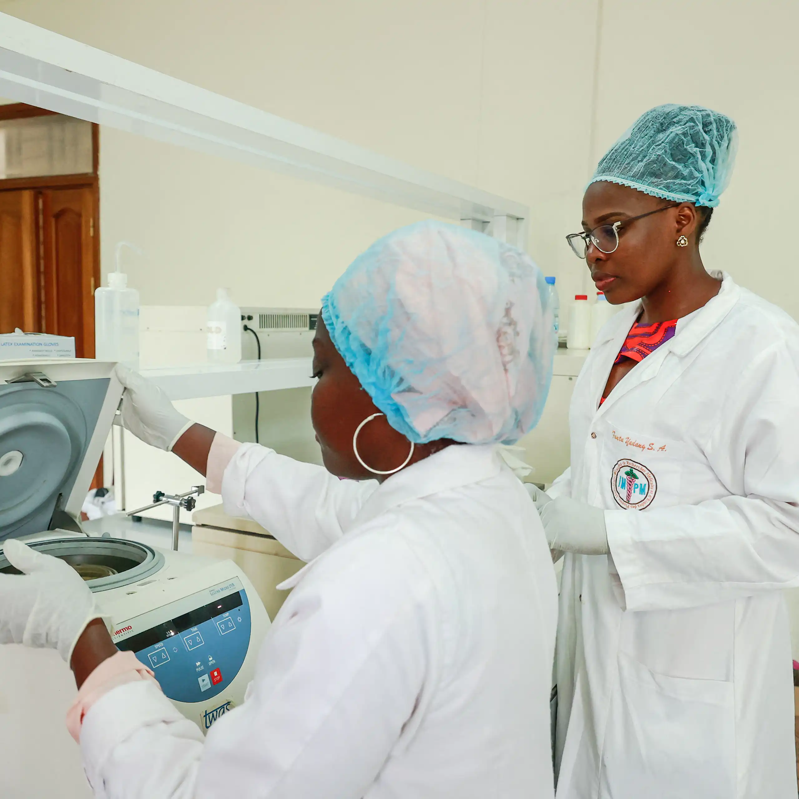 Two women wearing white coats, caps and gloves in a laboratory