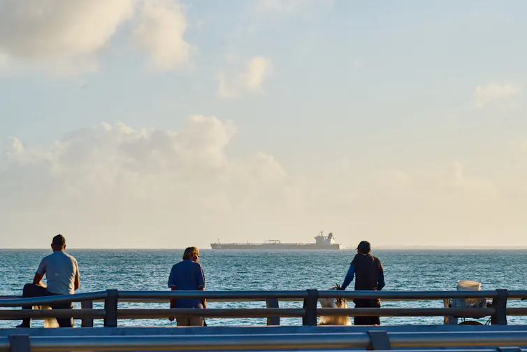 People look out to sea with oil tanker on horizon.