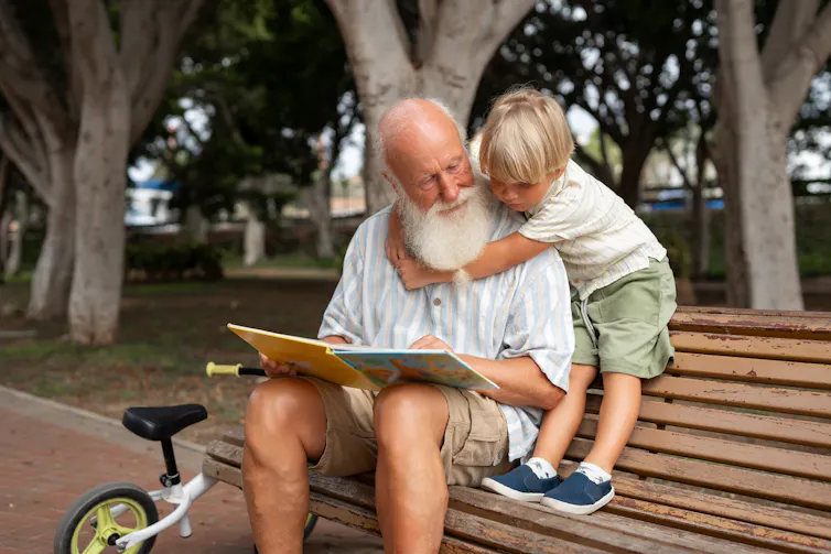 An old man and a young child reading a book together in a park.