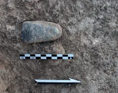 A curved stone lies on the ground, with a graphic of an arrow and a scale ruler.