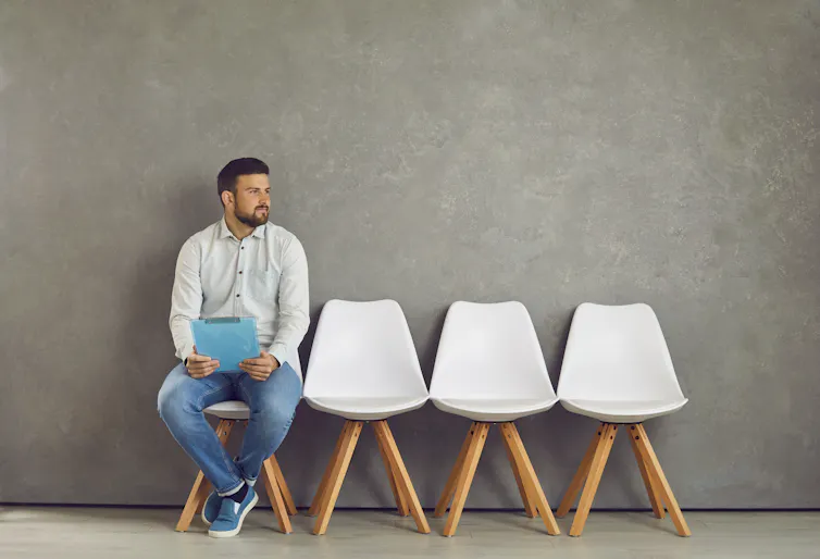 male candidate sitting on a chair at the end of a row while waiting for a job interview.