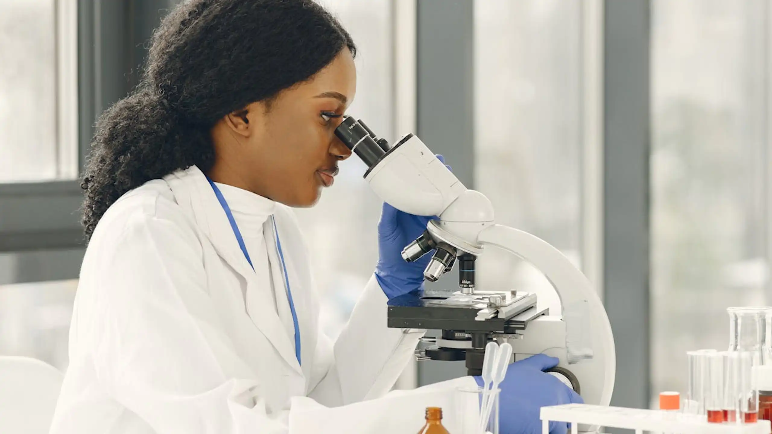 Woman in a white coat looking into a microscope