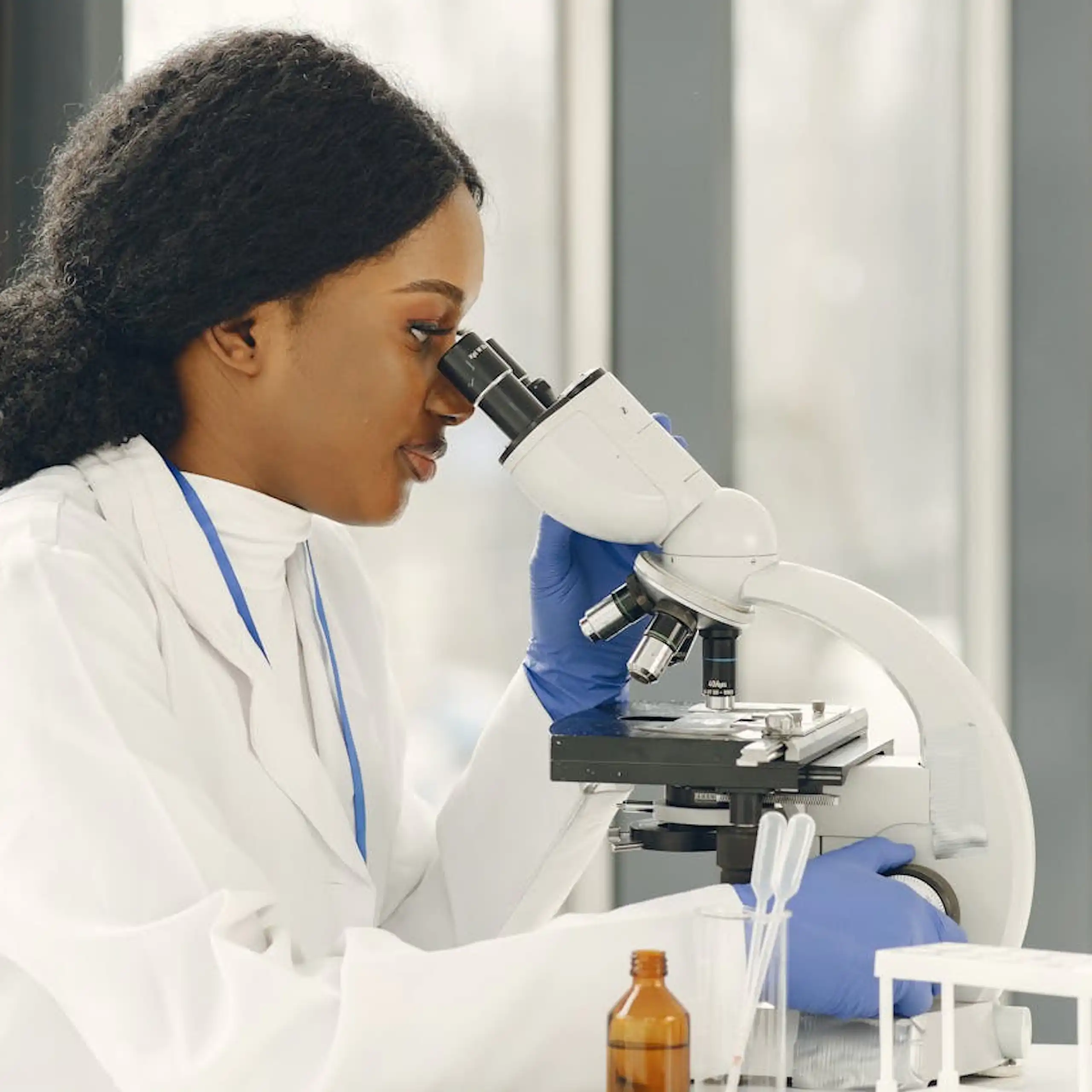 Woman in a white coat looking into a microscope