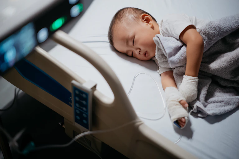 Baby in a hospital bed with an IV drip in his hand