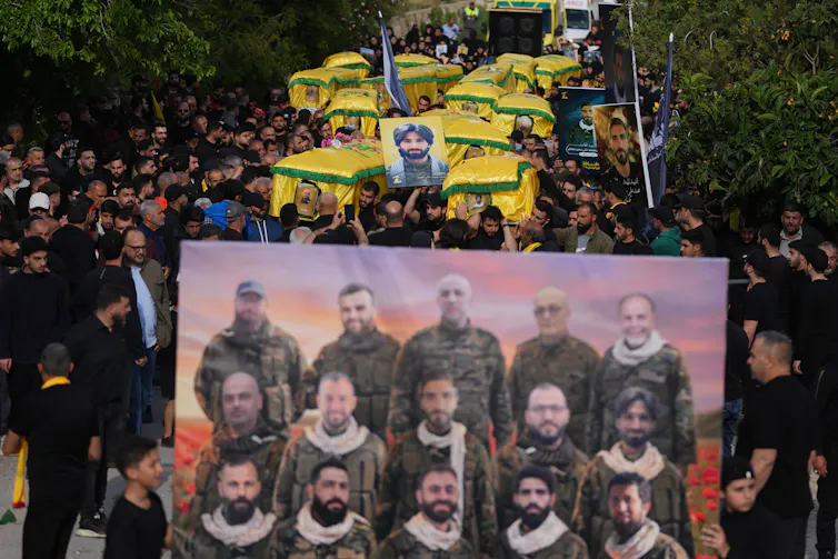 La "guerra justa" ha guiado el pensamiento católico sobre los conflictos durante siglos, incluidas las críticas a la guerra de Irán. 1 Una multitud de personas, muchas de ellas vestidas de negro, caminan sosteniendo ataúdes envueltos en tela amarilla y una gran fotografía de 15 hombres con uniformes militares.