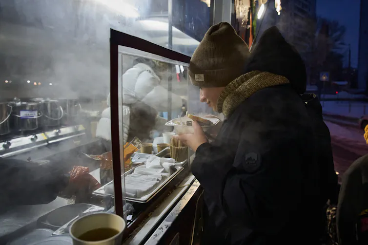 Someone stands in front of a steamed up window holding a bowl of soup.