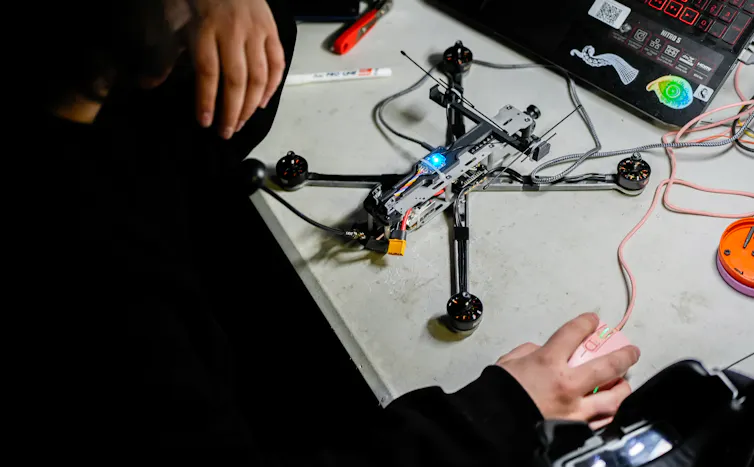 A drone on a table; a man's hands are visible on either side of it.