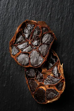 A bulb of black garlic cut in half to reveal the cross-sections of the cloves, which are black and softened.
