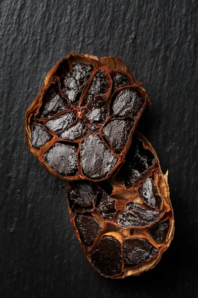 A bulb of black garlic cut in half to reveal the cross-sections of the cloves, which are black and softened.