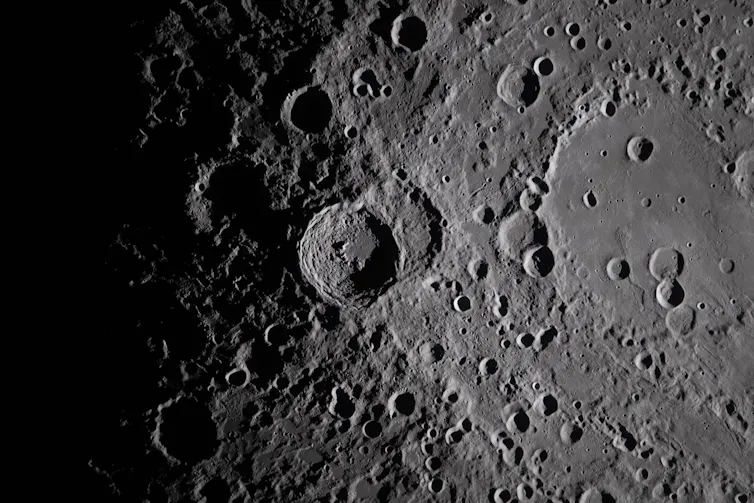 A closeup view of the moon's cratered surface, grey in colour.