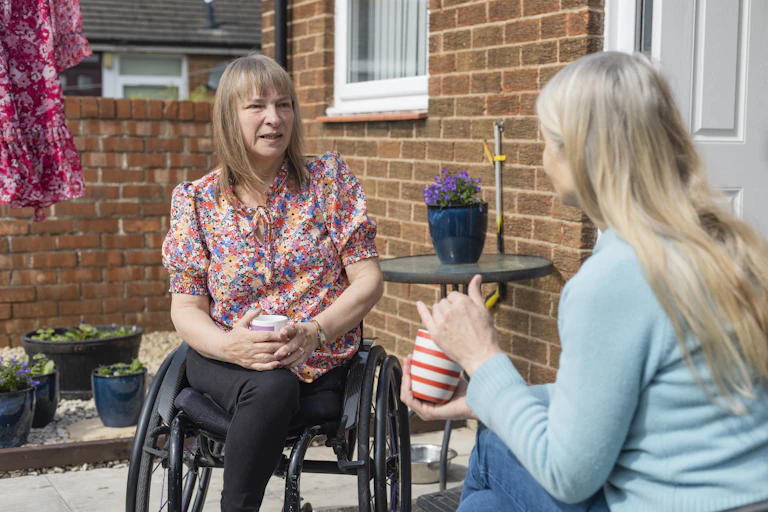 Disabled woman talks to a friend while drinking tea in her patio