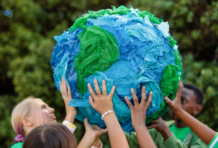 Several hands holding up a globe which appears to be made from blue and green fabric.