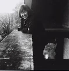 Fotografía en blanco y negro de una mujer sonriente apoyada en una barandilla.