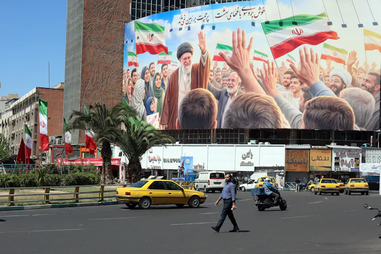 A man walks in front of a poster showing a crowd hailing former supreme leader Ayatollah Ali Khamenei.