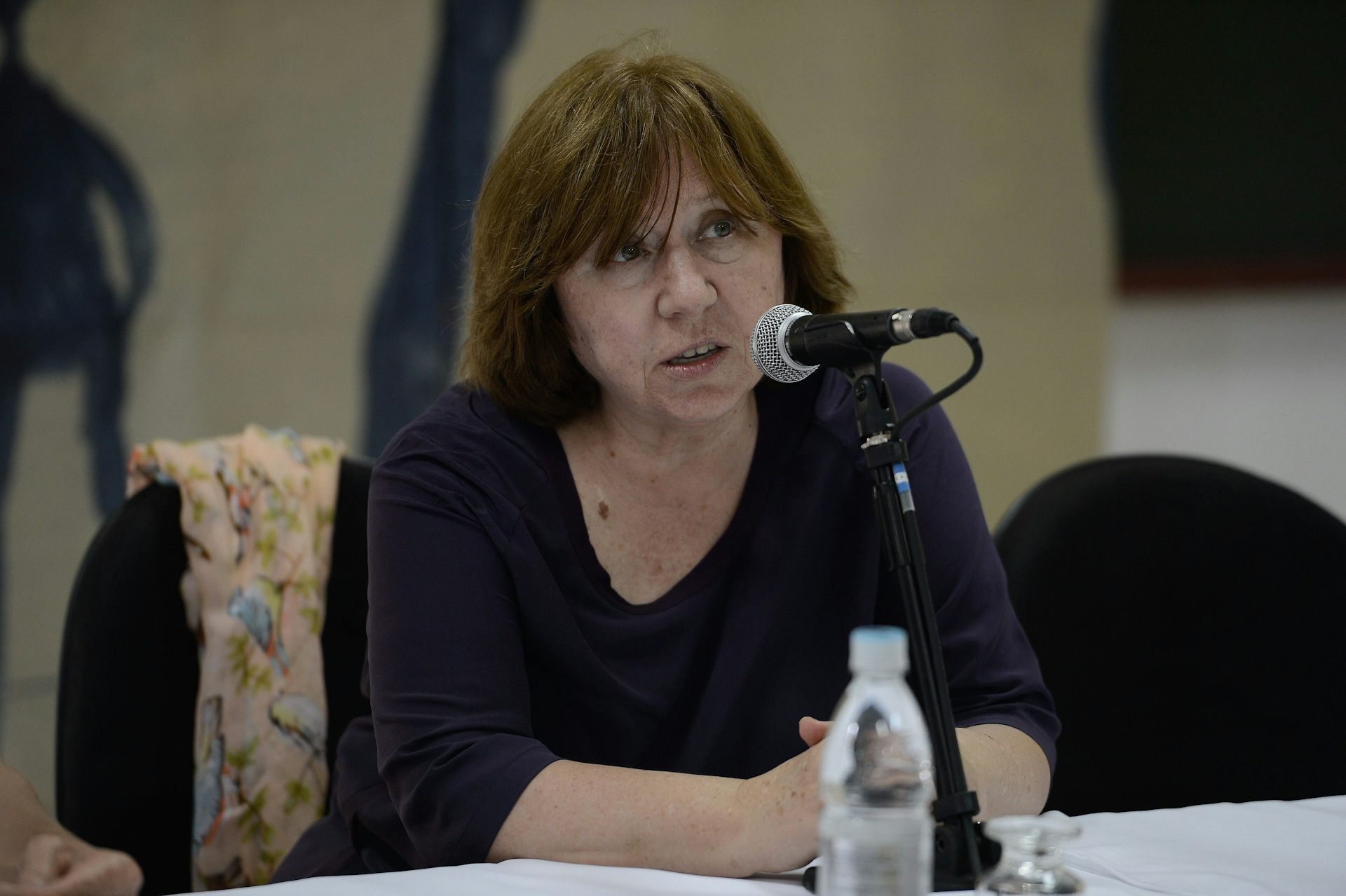 Una dona parla asseguda a una taula davant un micròfon.