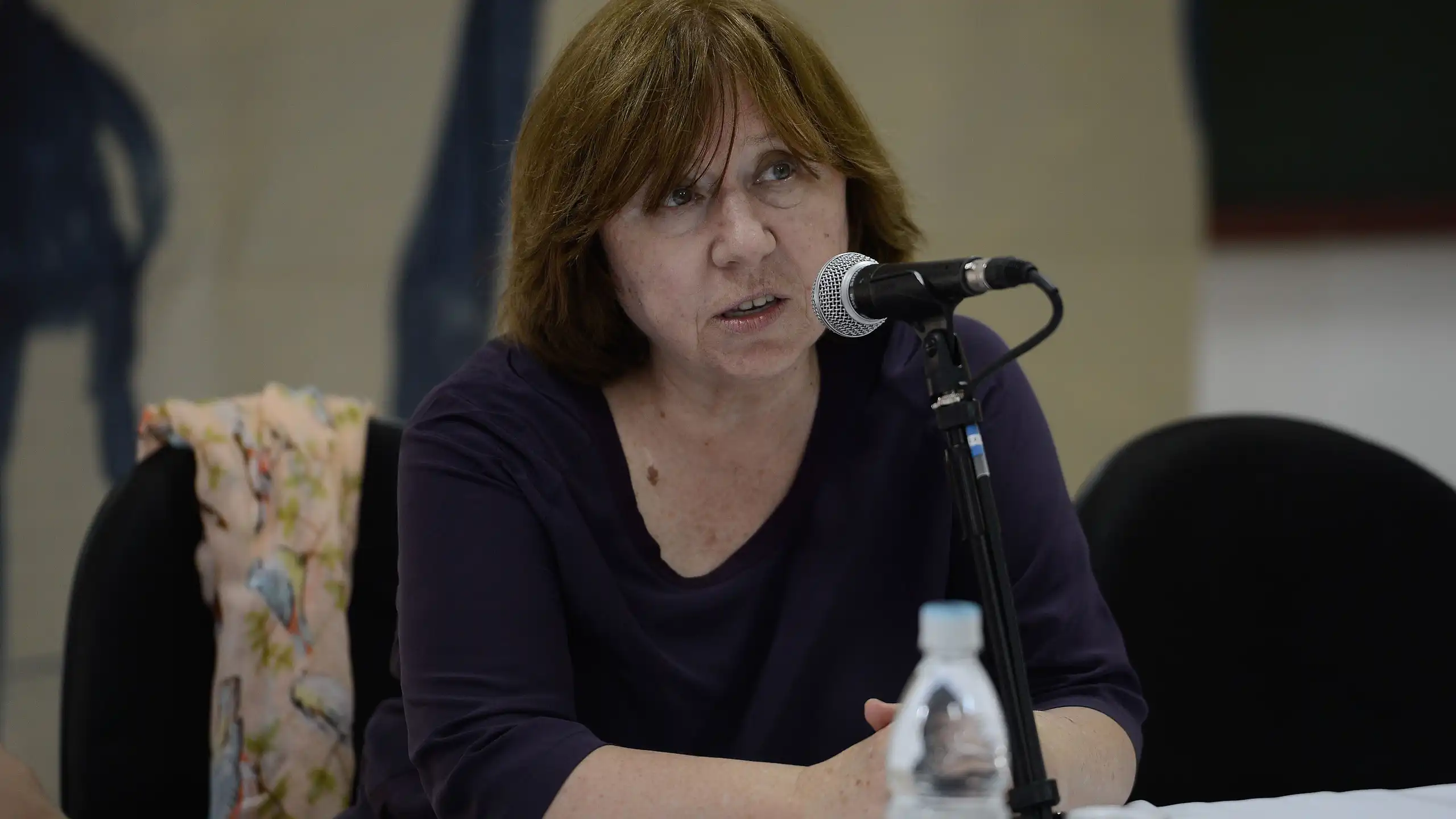 Una dona parla asseguda a una taula davant un micròfon.