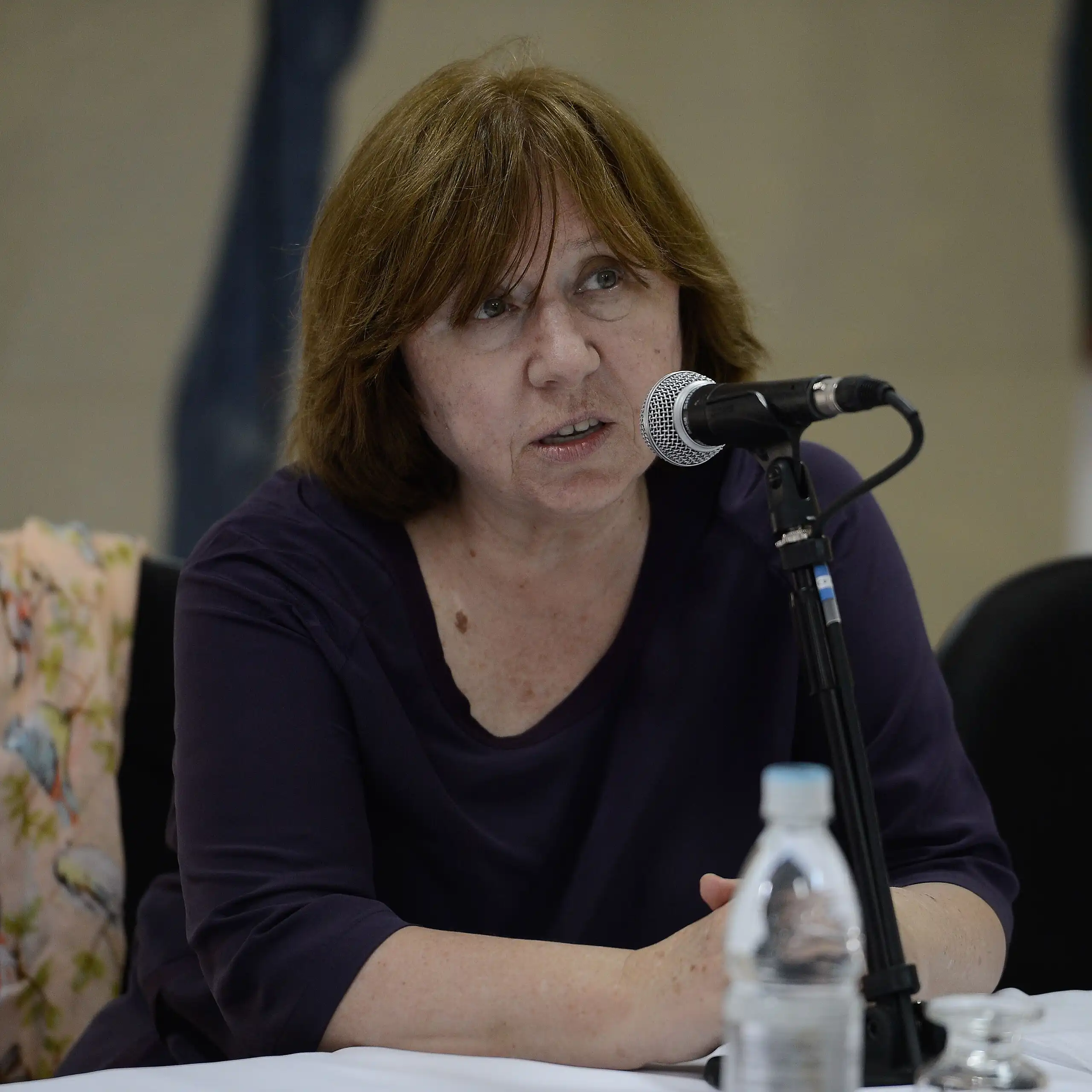 Una dona parla asseguda a una taula davant un micròfon.