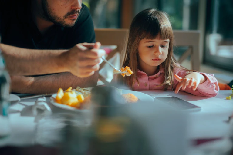 Une petite fille qui consulte un smartphone en déjeunant avec son père