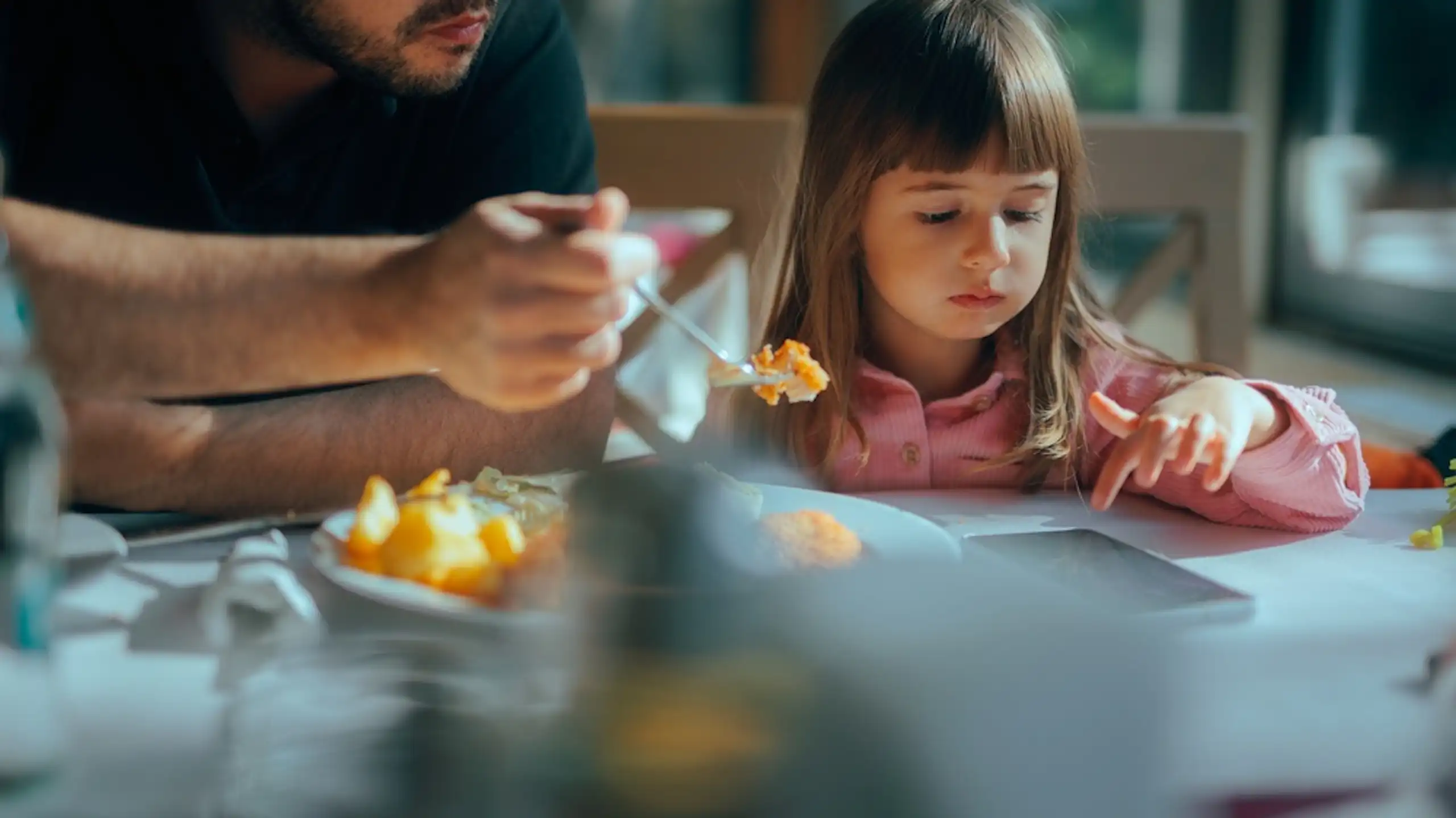 Une petite fille qui consulte un smartphone en déjeunant avec son père