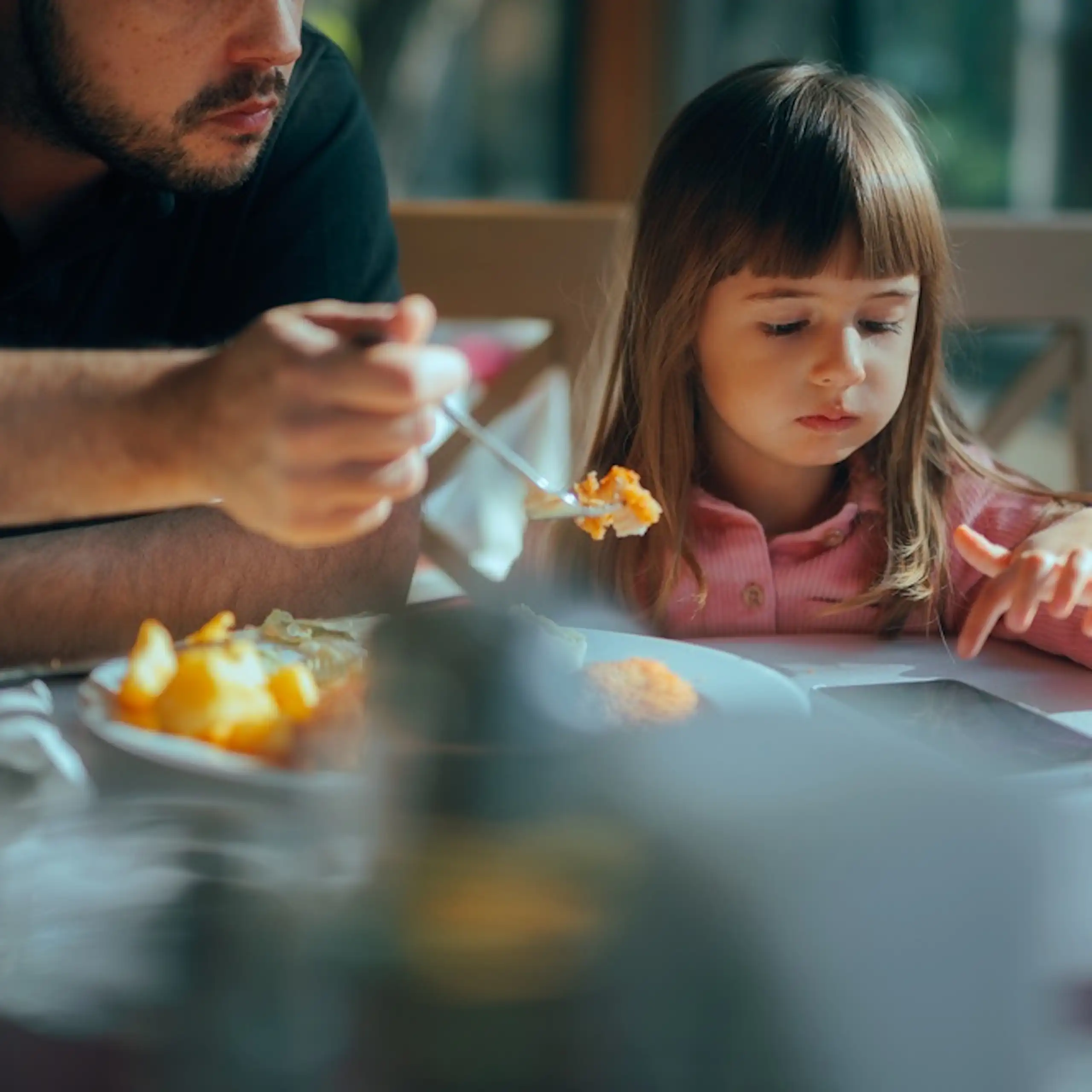 Une petite fille qui consulte un smartphone en déjeunant avec son père