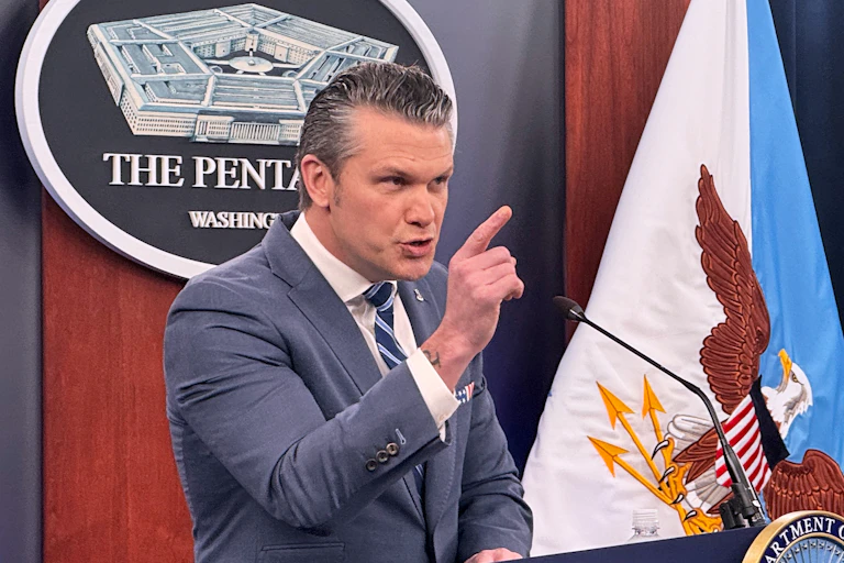 A man glowers with one hand raised as he stands behind a podium at a press briefing.