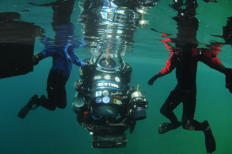 Astronaut diving in Pavilion Lake to study microbialites, supporting Curiosity rover Mars life research.