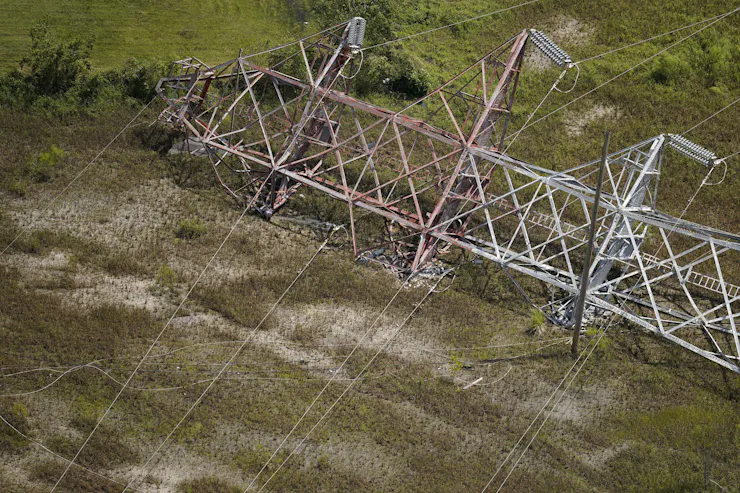A large transmission tower lies on its side, twisted, after a hurricane.
