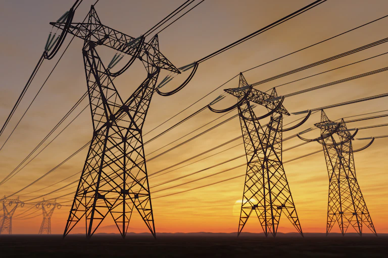 The silhouettes of a series of large transmission towers loom in the photo with the glow of the setting sun behind them.