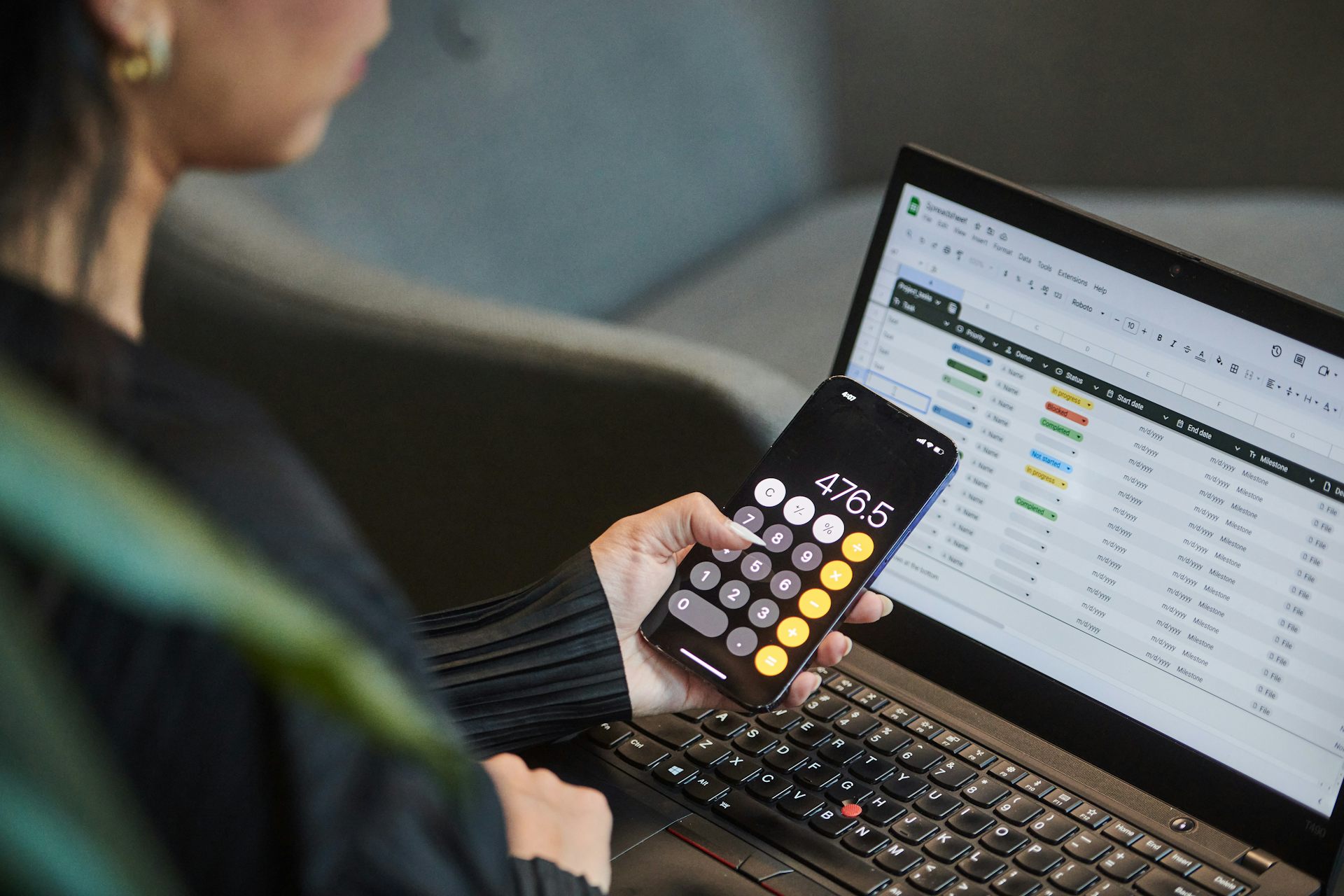 Una persona usa una aplicación de calculadora en su teléfono mientras trabaja en una hoja de cálculo