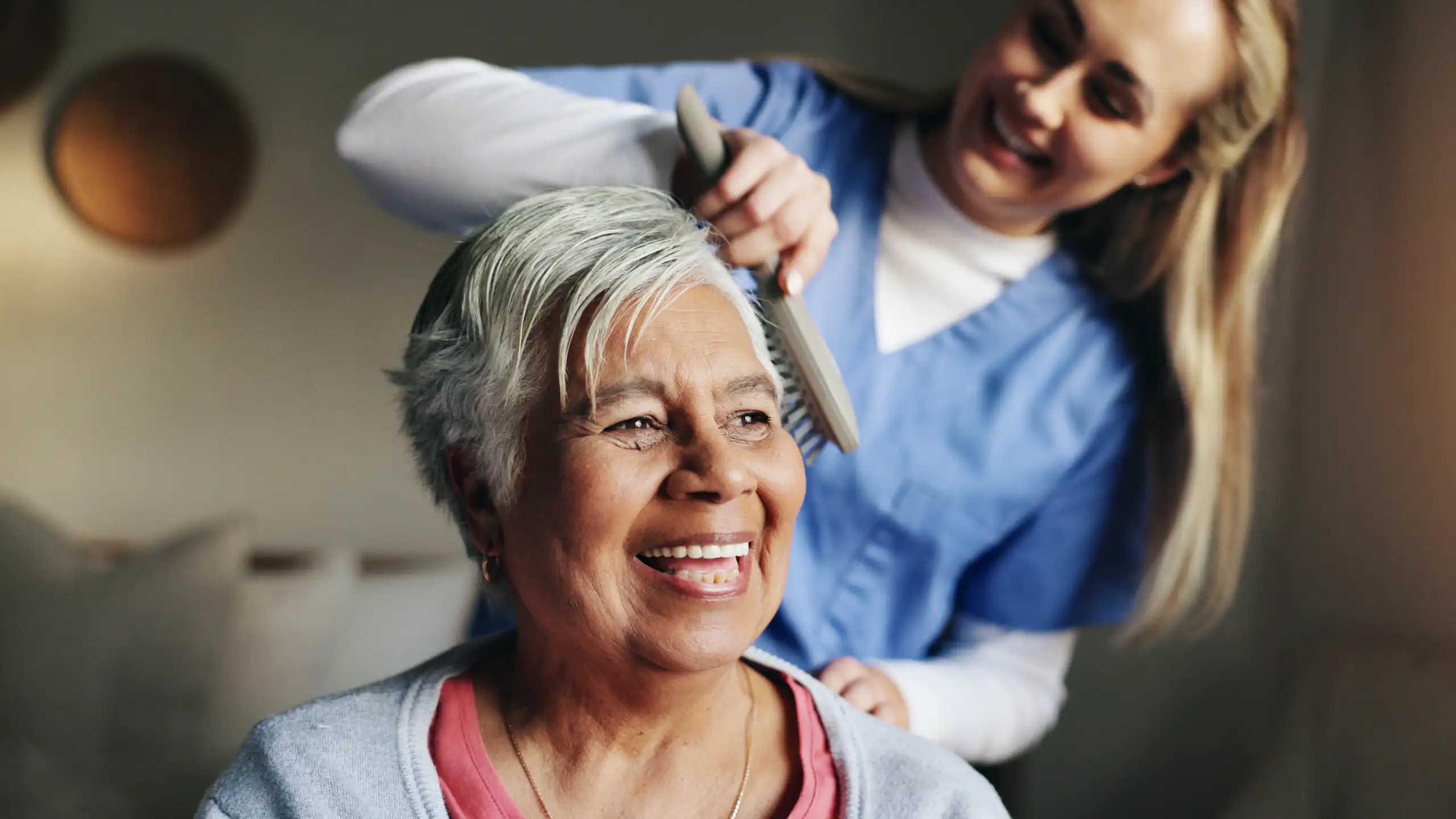 Nurse or Cader brushing hair of smiling elderly woman