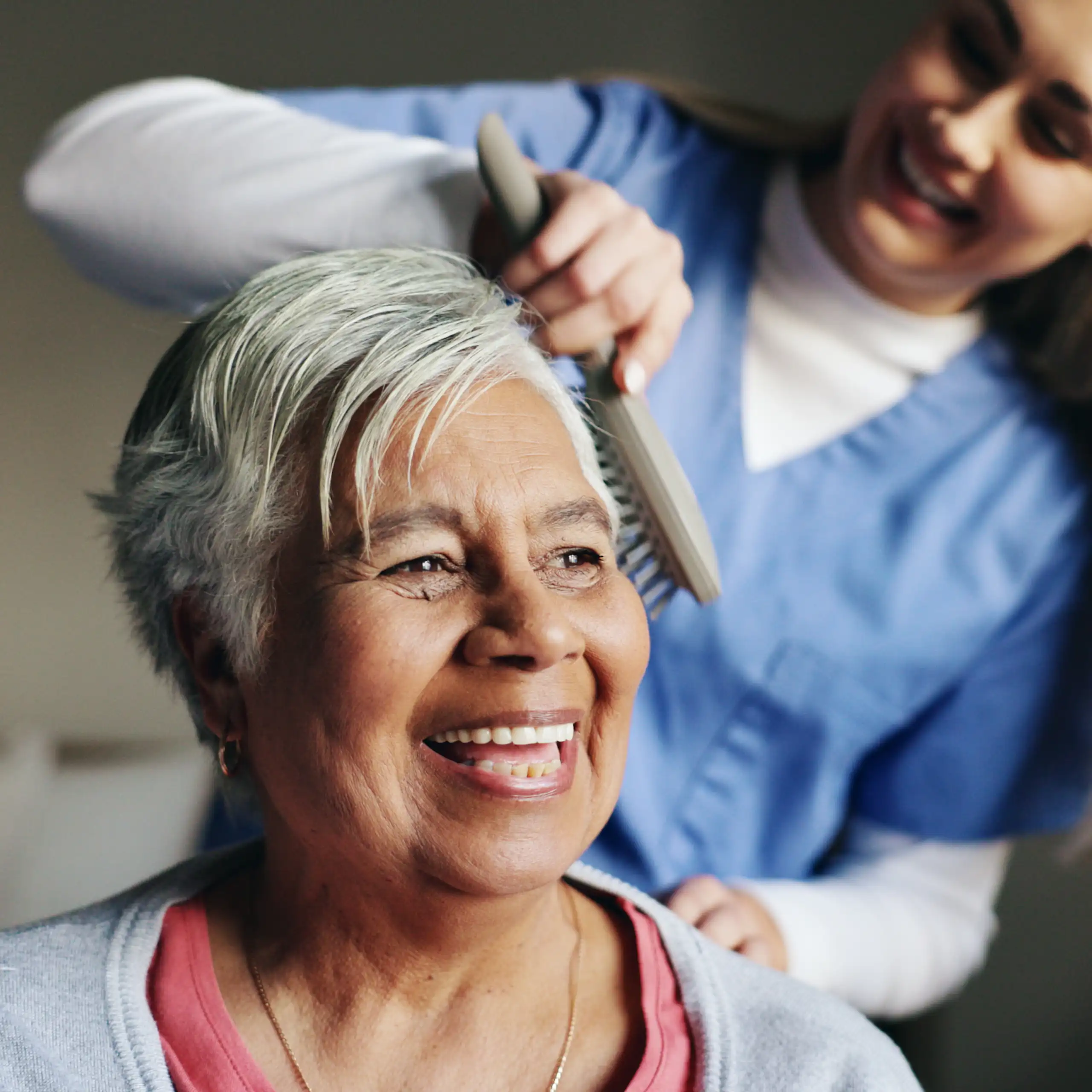 Nurse or Cader brushing hair of smiling elderly woman