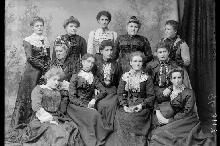 An old black and white photo shows Australian women suffragists, in dresses, posing in a group photo.