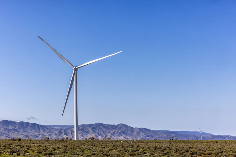 single wind turbine against blue sky, mountains in background
