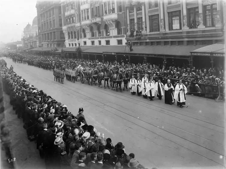 A crowd watches a procession down a Melbourne street.