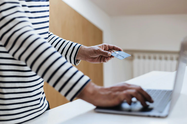 A person holding a credit card shopping online with a laptop