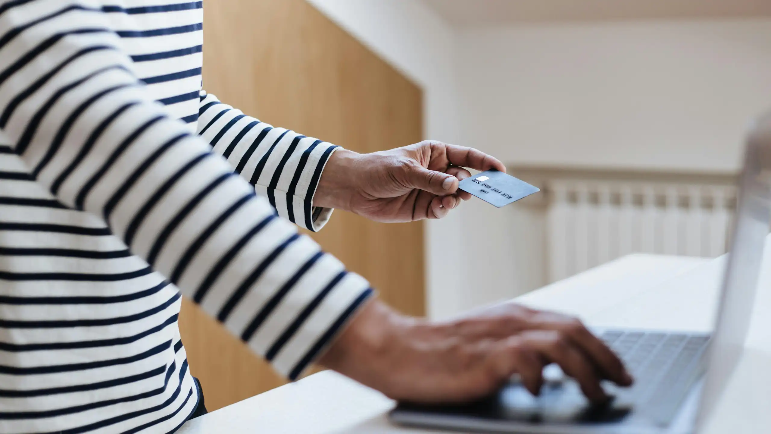 A person holding a credit card shopping online with a laptop
