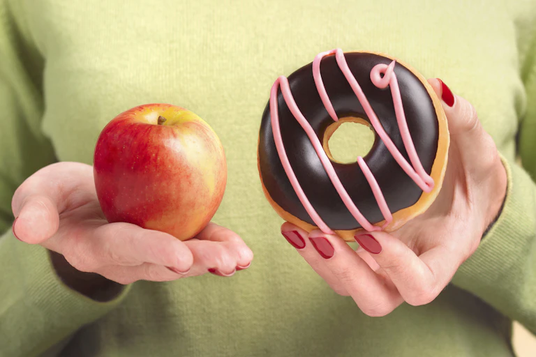 A person holds an apple in one hand and a donut in the other.