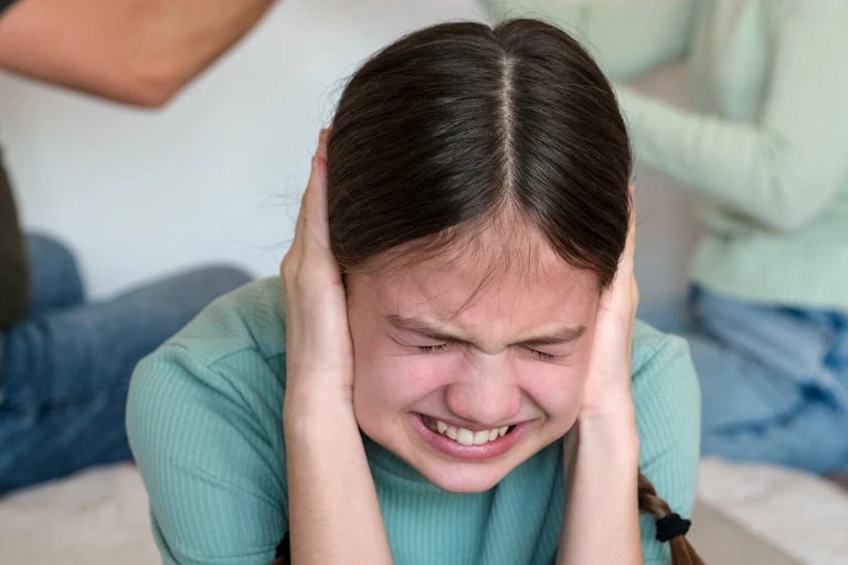 Una niña se tapa las orejas con las manos y cierra los ojos muy fuerte.