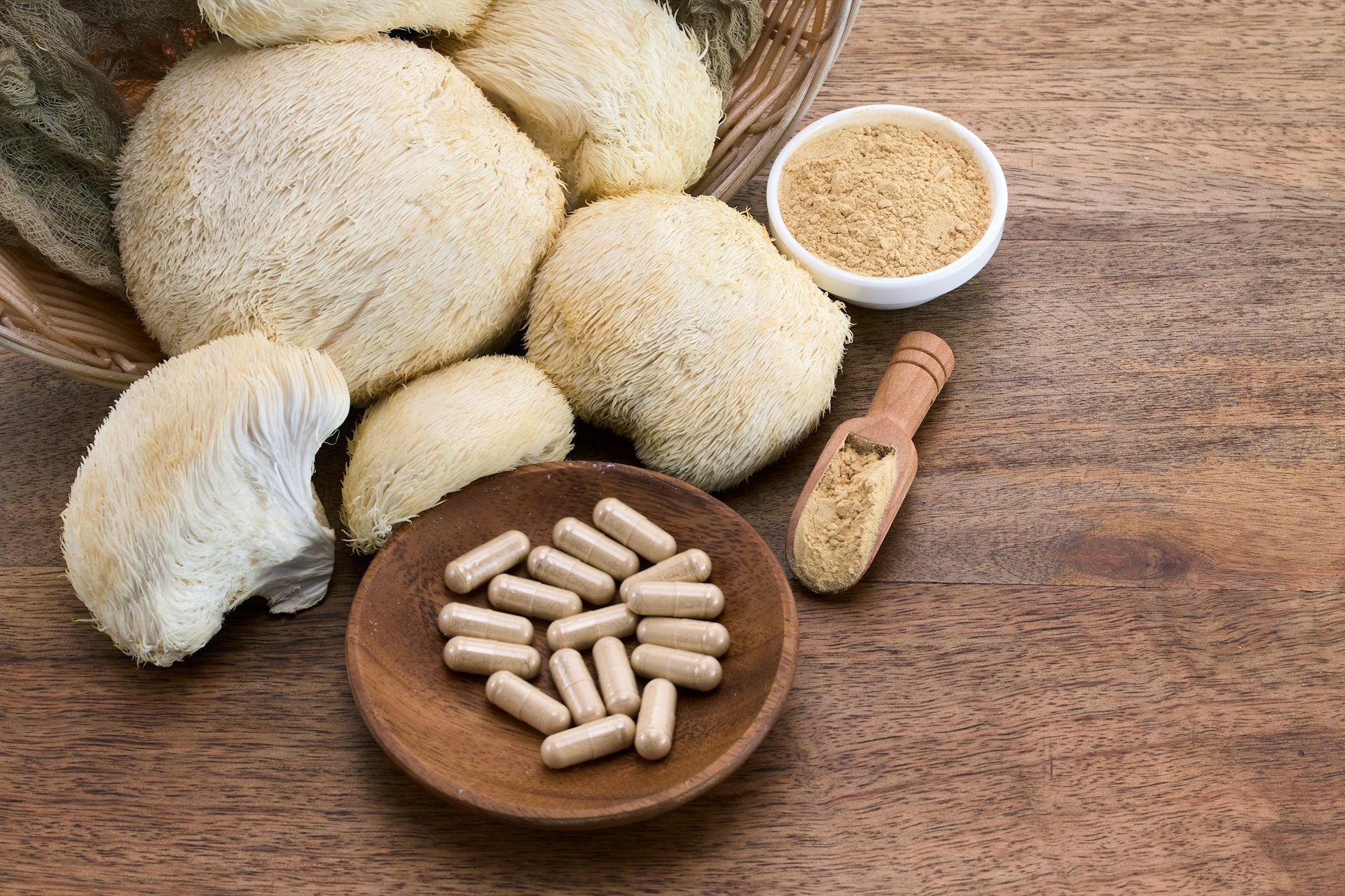 An bunch of lion's mane mushrooms arranged on a counter next to a dozen or so lion's mane mushroom supplements.