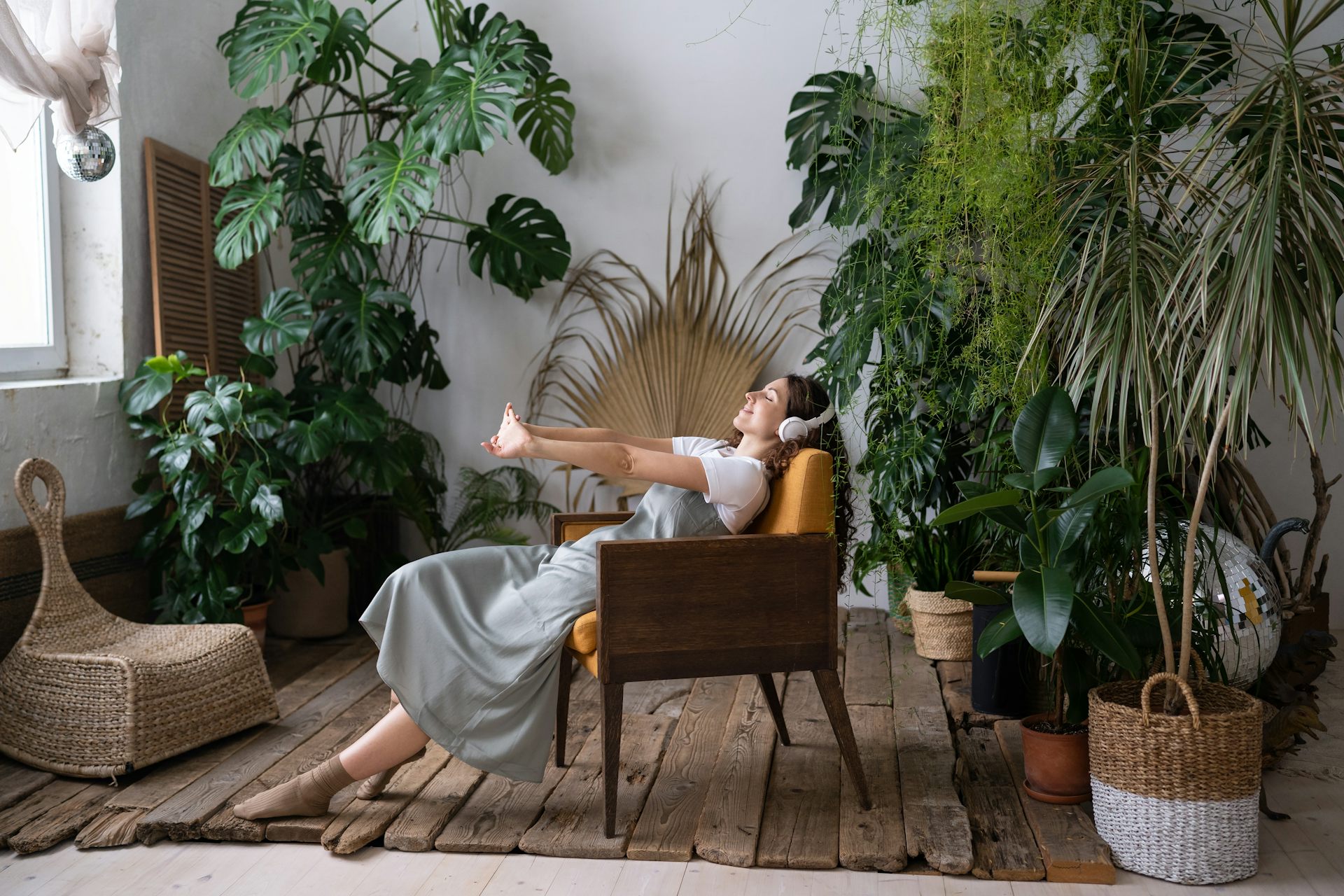 Woman wearing headphones leaning back in armchair, surrounded by large houseplants