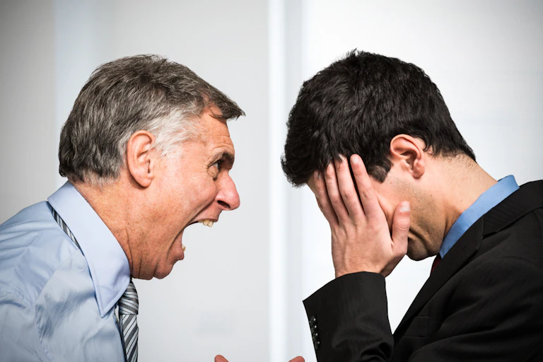 An older man shouting at a younger man in an office setting.
