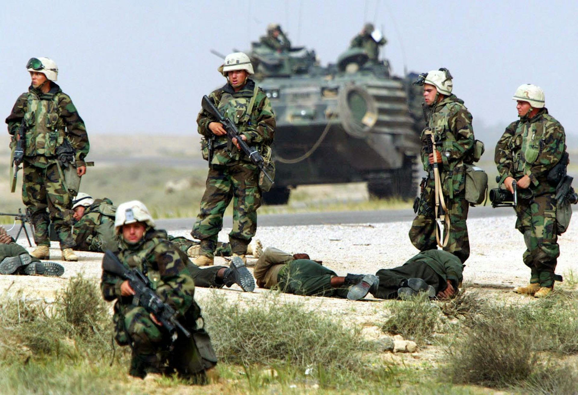 Soldados fuertemente armados rodean a los hombres que yacen en el suelo. Detrás de ellos hay un tanque.