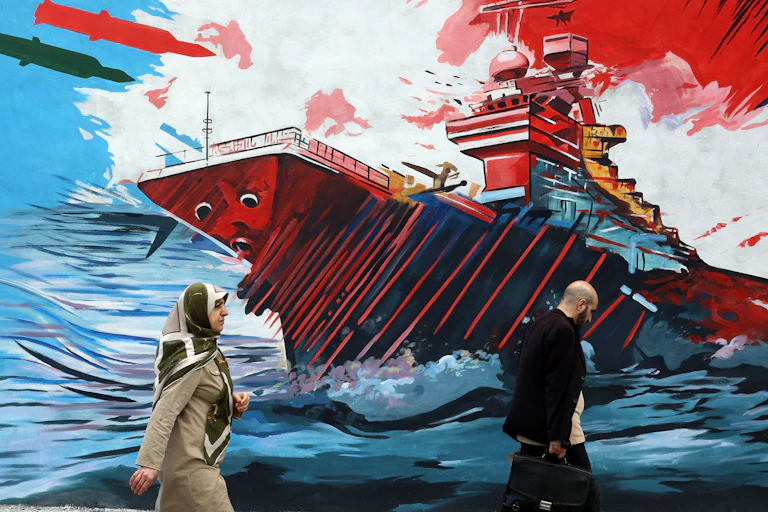 Iranians walk past a billboard depicting a US warchip under attack.