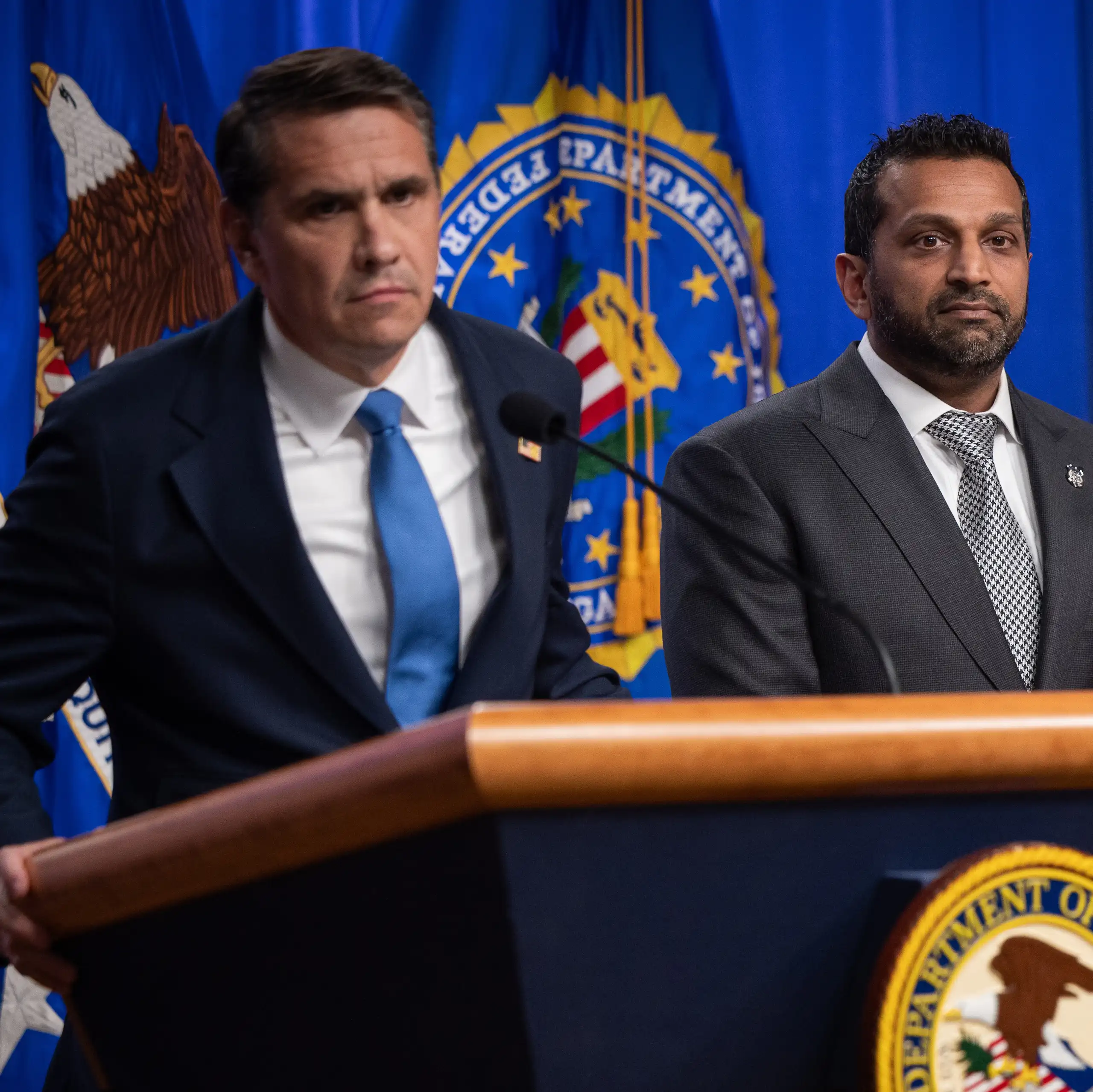 Two men stand at a lectern with an official U.S. seal emblazoned upon it.